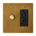 Brass wall plate with black electrical outlet and rotary dimmer on a white background